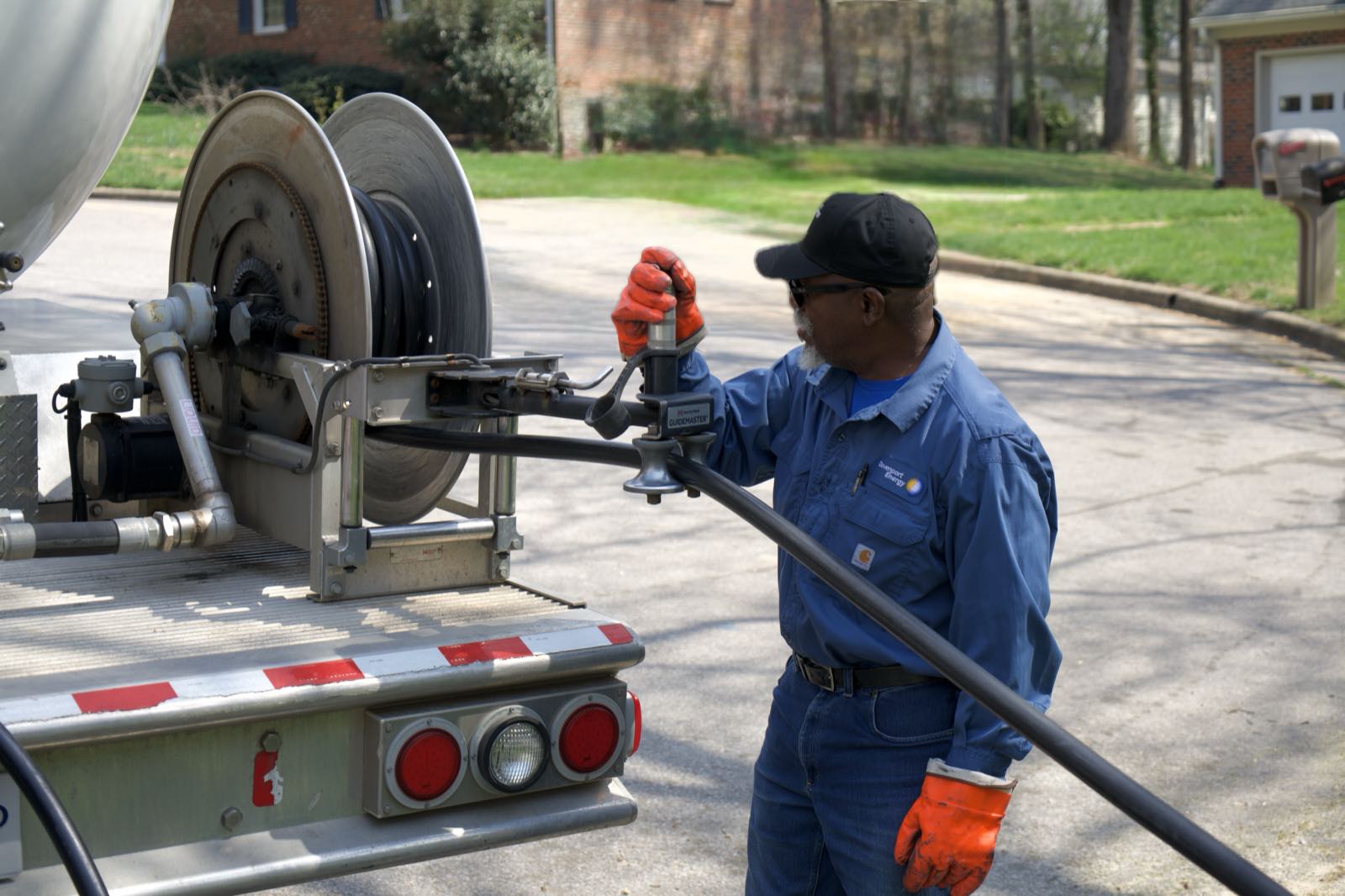 A Davenport Energy driver operating the delivery hose reel on a propane bobtail outside a home